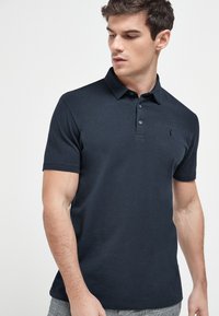 Navy Poloshirt aus Baumwolle mit einem Drei-Knopf-Verschluss und einem kleinen stickierten Logo auf der Brust. Kurze Ärmel, klassische Passform.