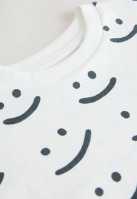 Hvid bomulds t-shirt med sorte smiley ansigt prints. Udhullet er ribbet, med en glat tekstur og almindelig pasform.