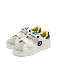 Zapatillas blancas y beige con correas de Velcro, que cuentan con un logo redondo azul, un forro interior amarillo y una suela de goma lisa.