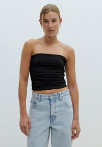 Zwarte strapless top met geplooide textuur, gecombineerd met lichtblauwe high-waisted jeans met vervaagde accenten en een relaxte pasvorm.