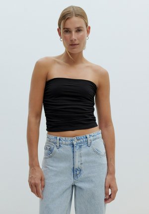 Schwarzes, trägerloses Oberteil mit geraffter Textur, kombiniert mit hellblauen, hochgeschnittenen Jeans mit verblassten Akzenten und einer lockeren Passform.