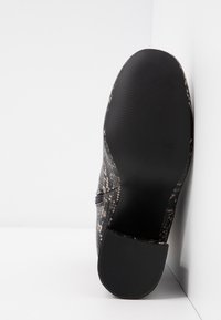 Chaussure noire texturée avec un motif en cuir de serpent, dotée d'une semelle en caoutchouc et d'une fermeture éclair sur le côté. Le dessous présente une surface striée pour une meilleure adhérence.