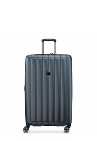 Valise rigide de couleur gris foncé, avec des rainures verticales, une poignée télescopique et quatre roulettes pivotantes pour la mobilité.