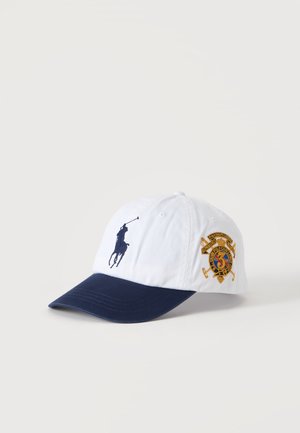 Hvid og navy baseballkasket med en polospillerlogo foran og et broderet våbenskjold på siden.