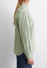 Camisa a rayas verdes y blancas con cuello, mangas largas y dobladillo curvo. Fabricada en tejido ligero con una textura suave.