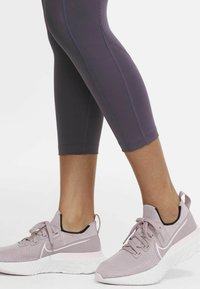 Baskets de sport rose clair avec un dessus en tissu texturé, fermeture à lacets et semelle extérieure blanche. Associées à des leggings ajustés violets foncés.