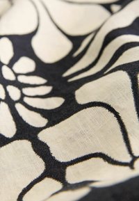 Czarny i kremowy materiał z dużym wzorem kwiatowym. Tekstura wydaje się gładka z delikatnym połyskiem, z wyraźnymi czarnymi konturami.