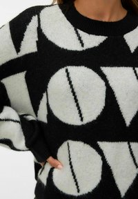 Maglione in bianco e nero caratterizzato da un audace design grafico con motivi circolari e linee diagonali, realizzato in materiale morbido e testurizzato.