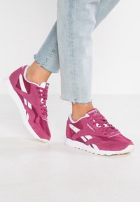 Fuchsie sportovní tenisky s bílými akcenty, s semišovým svrškem, kulatou špičkou a texturem gumovou podešví. Neformální design s šněrováním.