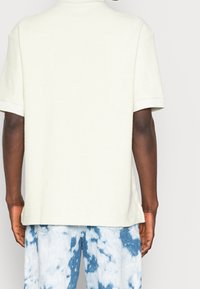 Krémová mikina z froté s krátkým rukávem, kulatým výstřihem a ohrnutými manžetami, spojená se světle modrými šortkami s tie-dye vzorem. Měkká textura, uvolněný střih.