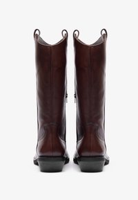 Bottes en cuir marron, montant jusqu'au genou, avec une finition lisse, des bouts ronds et des fermetures éclair sur le côté. Présentent une semelle texturée et des languettes de tirage en haut.