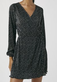 Robe noire portefeuille à manches longues, avec des rayures verticales blanches et de petits pois, en tissu texturé et détail de taille froncée.