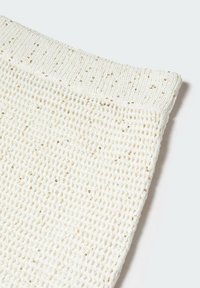 Tessuto a maglia di colore crema con una trama aperta e testurizzata, caratterizzato da piccole paillettes dorate sparse sulla superficie.