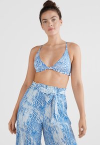 Top de biquíni azul e branco com padrão em forma triangular e alças finas, combinado com calças soltas de cintura alta com um nó na cintura.