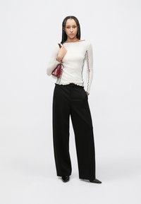 Top alb cu mâneci lungi și margini negre ondulate, asortat cu pantaloni negri lejeri și o geantă mică burgundy. Pantofi negri cu vârf ascuțit.