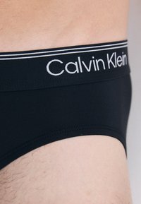 Schwarze Baumwoll-Boxer-Briefs mit einem weißen Calvin Klein-Logo auf einem kontrastierenden Bund, mit glatter Textur und enger Passform.