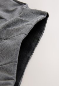 Tissu textile gris à texture lisse, avec une doublure intérieure noire côtelée au bord. Le design est contourné et ajusté.