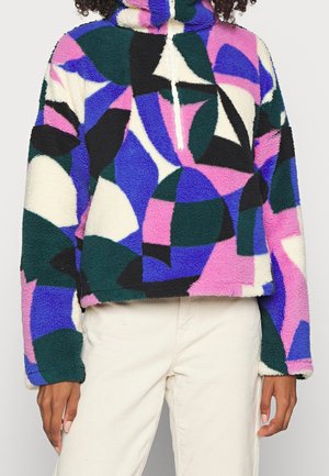 Sudadera con capucha de forro polar con patrón abstracto multicolor y cordón blanco, usada con pantalones beige claro.