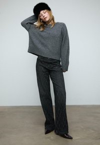 Szary, krótki sweter dzianinowy w zestawieniu z szerokimi, czarnymi dżinsami z wzorem w romby. Modelka nosi czapkę z czarnego futra oraz spiczaste burgundowe szpilki.