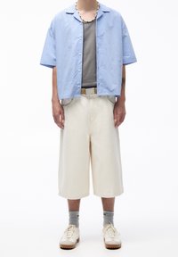 Koszulka z krótkim rękawem w niebieskie paski na szarym podkoszulku, połączona z kremowymi kulotami i beżowymi sneakersami. Cechy to dopasowany krój i swobodny styl.