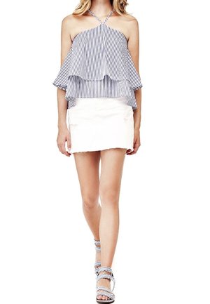 Haut dos nu rayé avec volants superposés, associé à une mini-jupe blanche. Des sandales à brides avec des accents métalliques complètent le look.