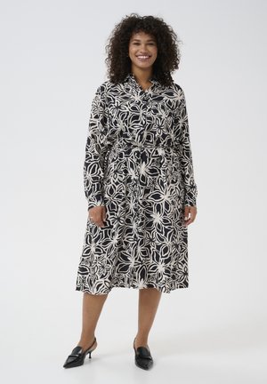 Button-up dress featuring a black and white floral pattern, long sleeves, a tie waist, and calf-length skirt. Paired with black heeled shoes.
