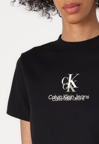 Černé bavlněné tričko s kulatým výstřihem, krátkými rukávy a předním potiskem s textem "Calvin Klein Jeans" a stylizovaným logem v bílé barvě.