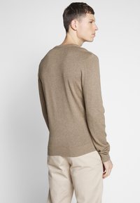 Suéter marrón de lana con mangas largas, escote redondo y dobladillo acanalado. La tela parece suave y tiene una textura lisa. Se lleva con pantalones de un color beige claro.