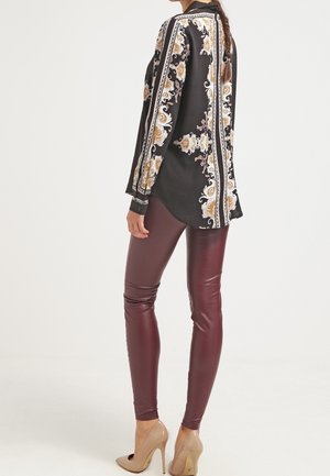 Blouse noire à manches longues avec un motif floral paisley et des rayures blanches ; associée à un legging en cuir bordeaux et des talons hauts couleur nude.