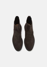 Botine Chelsea din suede maro închis, cu un inserts din piele netedă, panouri laterale elastice și detalii decorative de brogue pe vârful încălțămintei.