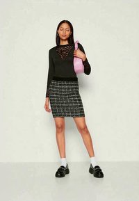 Mulher com um top de renda preto e uma saia xadrez preto-e-branco segura uma bolsa rosa ao ombro, vestindo meias brancas e sapatos de plataforma pretos.