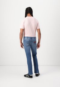 Camisa de manga corta color rosa claro combinada con jeans de denim azul. Los jeans presentan un diseño clásico de cinco bolsillos y una etiqueta de cuero marrón en la parte trasera.