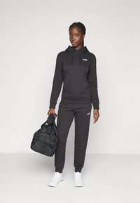 Set di felpa nera e pantaloni da tuta con logo PUMA, realizzato in materiale morbido. Abbiamo abbinato a delle sneakers bianche e a una borsa a tracolla nera.
