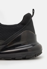 Svart idrottssko med ovandel i mesh, slät gummihäl, texturerade detaljer och en vadderad sula med en lätt kurva.