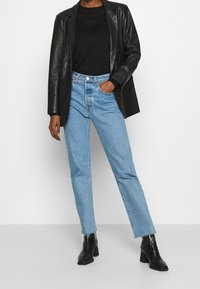 Svart läderblazer, svart topp, ljusblå raka jeans med rå kant och svarta klackade ankelstövlar.