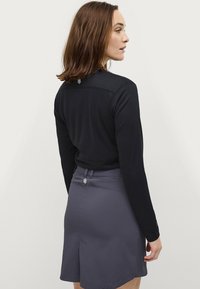 Zwarte top met lange mouwen en een gestructureerde afwerking, voorzien van een logo op de achterkant, gecombineerd met een lichte, grijze rok tot de knieën met een zijsplit.