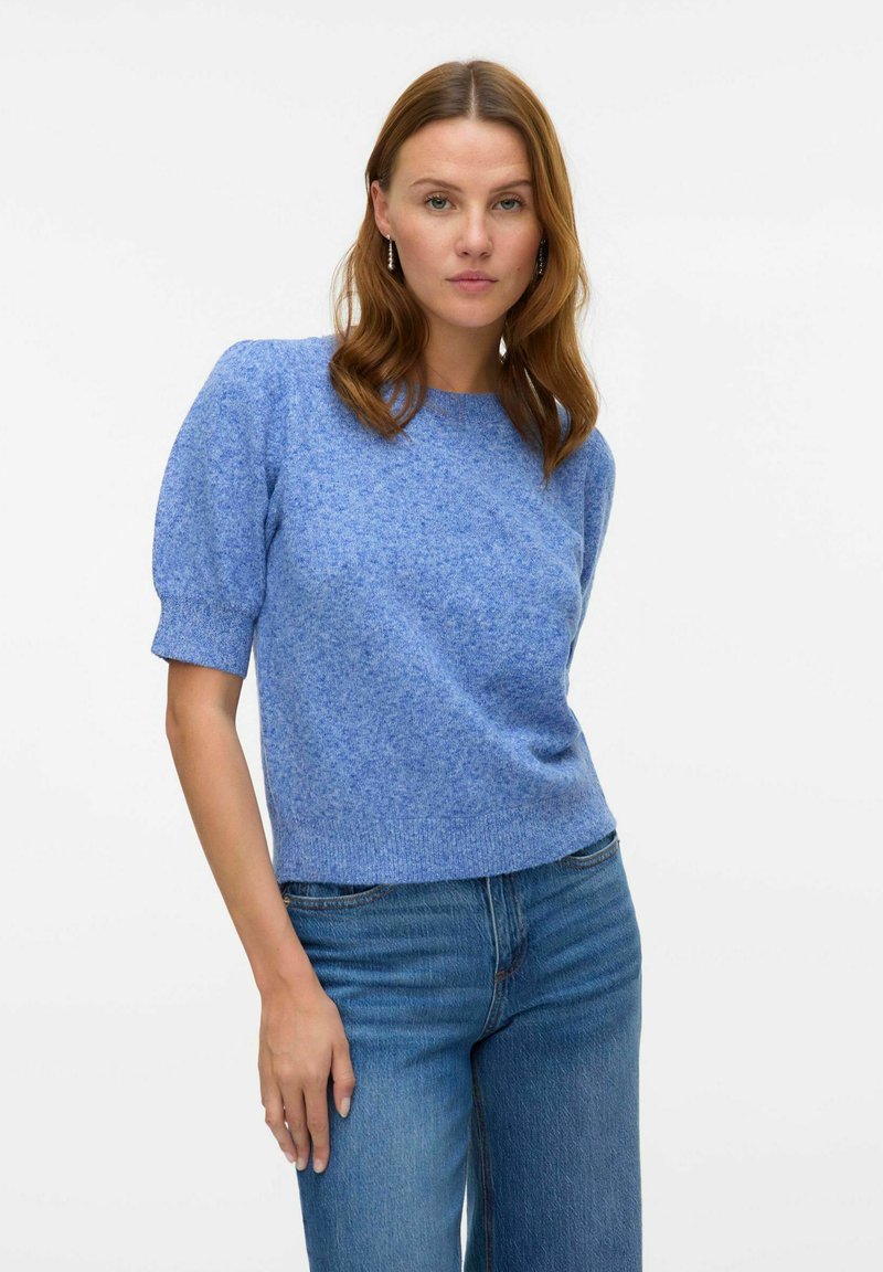 Pull en bleu clair, texturé, avec des manches courtes et bouffantes et un col rond, assorti à un jean bleu clair.