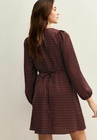 Vestido burdeos con estampado de lunares, mangas largas estilo globo, cintura ajustada con lazo y falda acampanada. Tejido ligero con un brillo sutil.