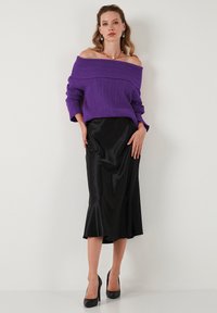 Maglione viola a coste con spalle scoperte, gonna midi in satin nera e tacchi alti neri. Il contrasto di un tessuto lavorato a maglia e un tessuto liscio crea uno stile unico.