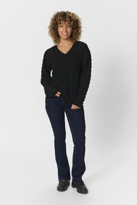 Maglione nero lavorato a maglia con scollo a V e motivo a punto aperto, abbinato a jeans a zampa d'elefante blu scuro e scarpe nere robuste.