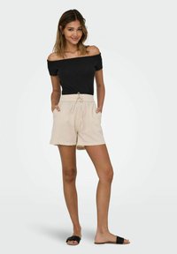 Sort off-shoulder top parret med beige linned shorts med elastisk talje og sidelommer. Båret med sorte slidesandaler.