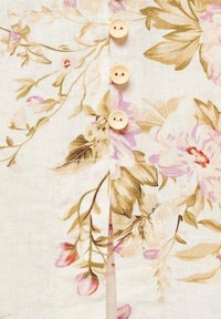 Světlá květinová látka s béžovými a růžovými odstíny, se svislým zapínáním na čtyři světle dřevěné knoflíky.