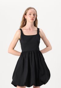 Μαύρο αμάνικο φόρεμα με τετράγωνη λαιμόκοψη, εφαρμοστό κορσέ και φούστα με πτυχώσεις που δημιουργεί στρογγυλή σιλουέτα. Λείο υλικό.