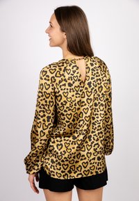 Long-sleeve blouse in satin with a leopard print featuring heart shapes. Gold background with black patterns and a keyhole back detail.
