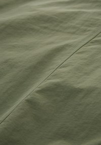 Ljust grönt tyg med en slät textur, med subtila vecken och en rak söm längs en söm, som förmedlar en mjuk, matt yta.