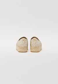 Beige espadrilles ar strukturētu auduma augšdaļu, kas rotāta ar atkārtojošos logotipa rakstu, dabīgu jutu apvalku un zeltītu aparatūru.
