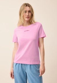 Camiseta de algodón rosa con mangas cortas que presenta "sono felice" bordado en rojo. Diseño sencillo con cuello redondo, combinada con vaqueros sueltos de color azul claro.
