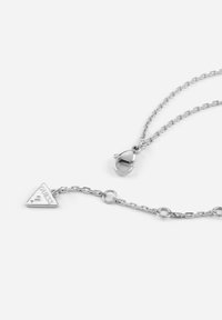 Collana in argento con pendente a triangolo inciso "Guess." Include un gancio a granchio e un design a maglia ovale. Texture liscia, stile minimalista.