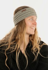 Bandeau en tricot gris clair, avec une texture en côtes horizontales et une petite étiquette en cuir marron. Convient pour une utilisation par temps froid.