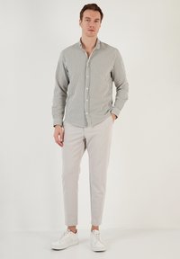 Camisa de rayas de manga larga en blanco y verde, con cuello abotonado y corte ajustado. Combinada con pantalones tapered en gris claro y zapatillas blancas.